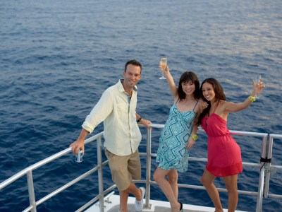 A man and two women drinking on the Big Sunset Cruise as the sun sets over the blue water in Tumon, Guam