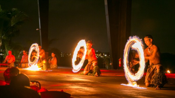 Three fire dancers kneeling and twirling fire at TaoTao Tasi in Tumon, Guam