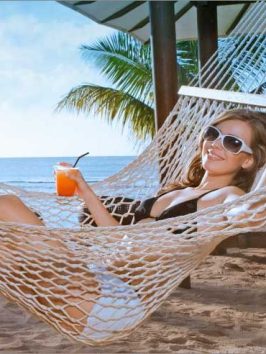 A girl lounging in a hammock with a cocktail in hand on the beach in Tumon, Guam