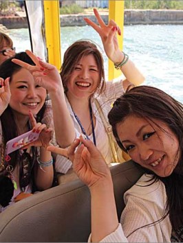 Three women holding up peace signs and smiling aboard Ride the Duck boat in Tumon, Guam