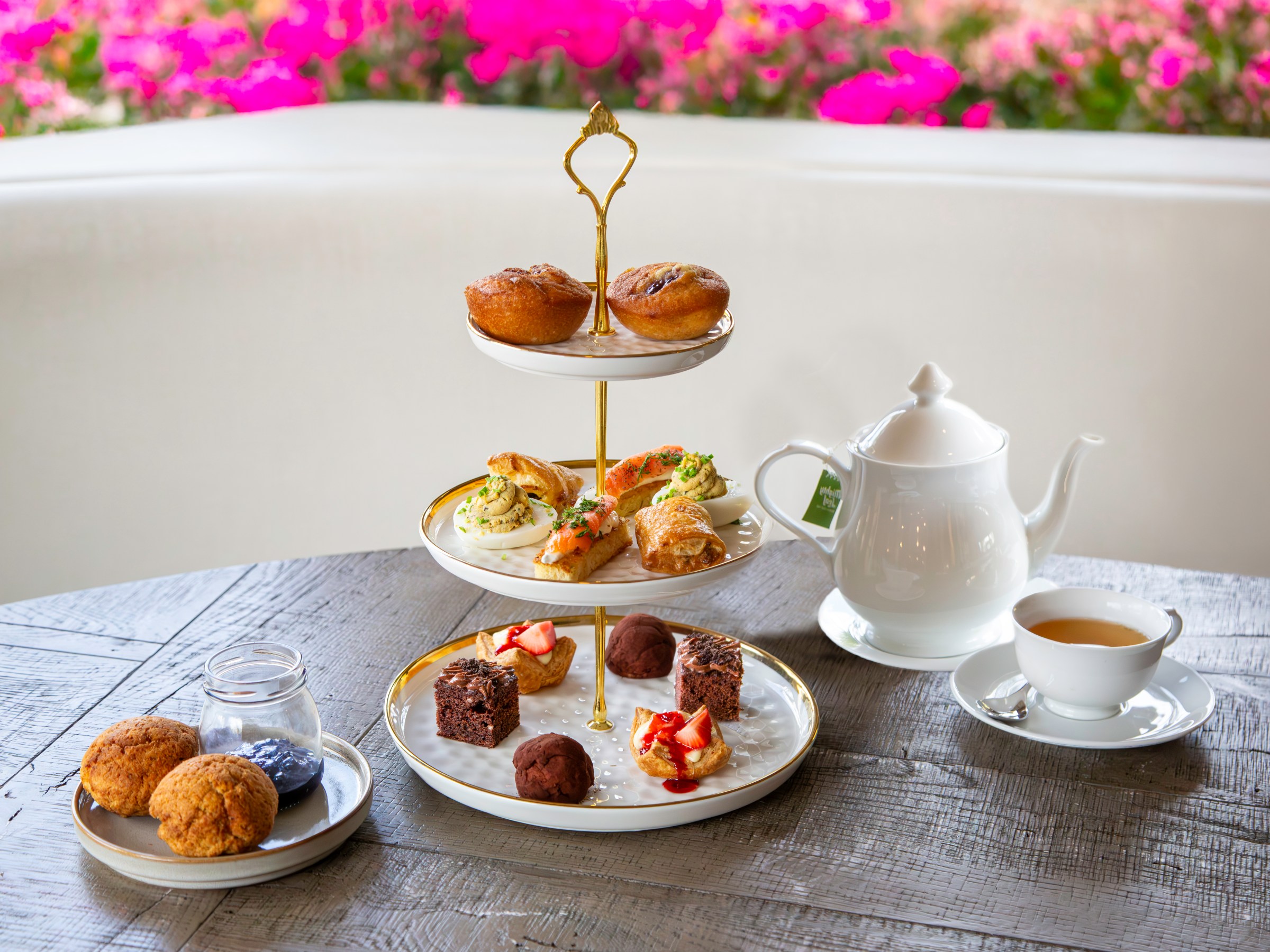 Three-tiered stand with pastries, a teapot, and teacup on a wooden table.