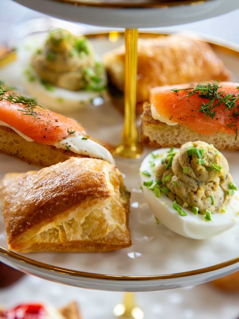 Tiered platter with smoked salmon on bread, deviled egg, and pastry.