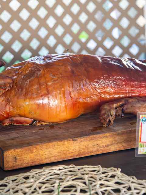 Whole roasted pig on a wooden board labeled 'Roast Pig' in multiple languages.