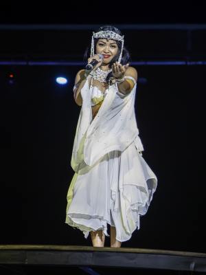 Performer in white costume sings on stage under dramatic lighting.