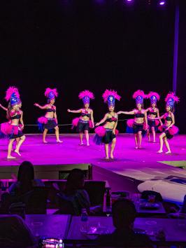 Dancers in bright costumes performing on stage with audience watching.