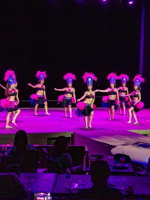 Dancers in bright costumes performing on stage with audience watching.