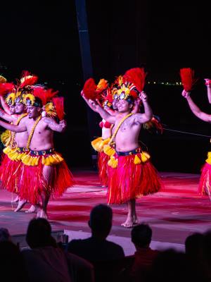 Traditional dancers in colorful attire perform on stage at night with an audience watching.