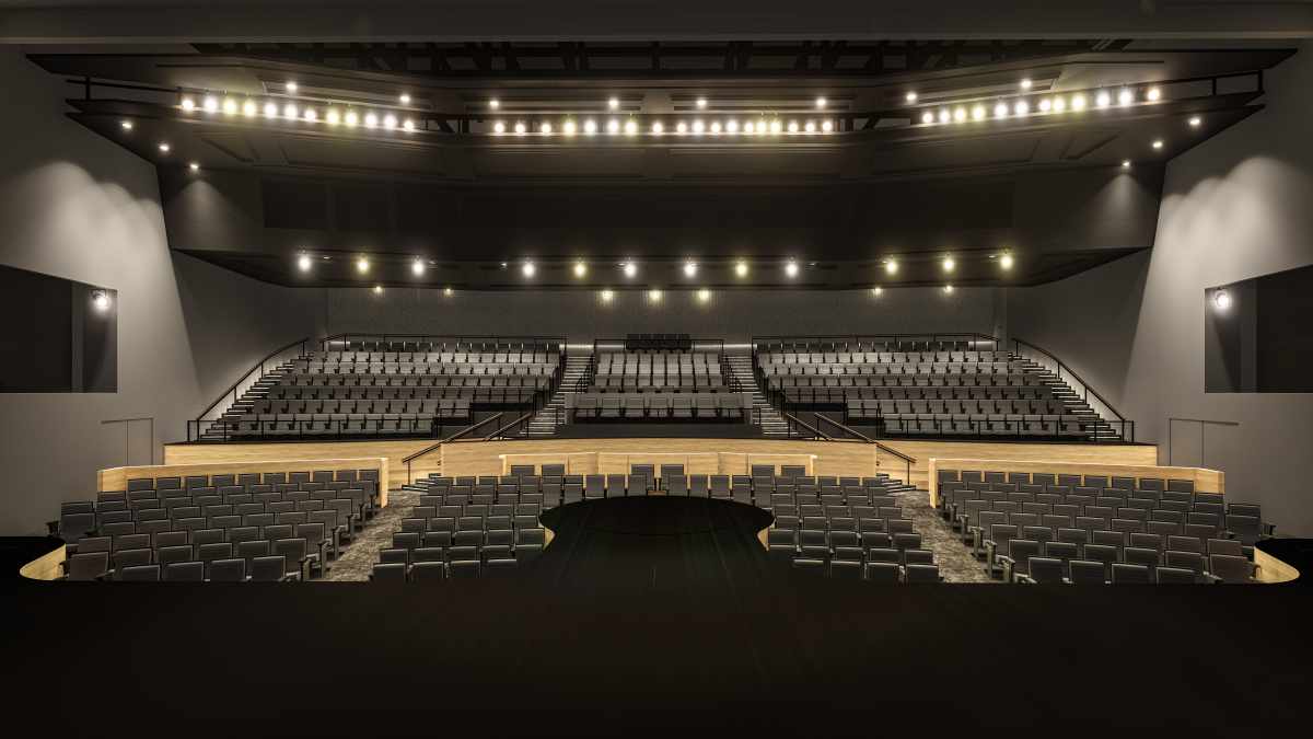 Empty auditorium with a stage, rows of seats, and overhead lights.
