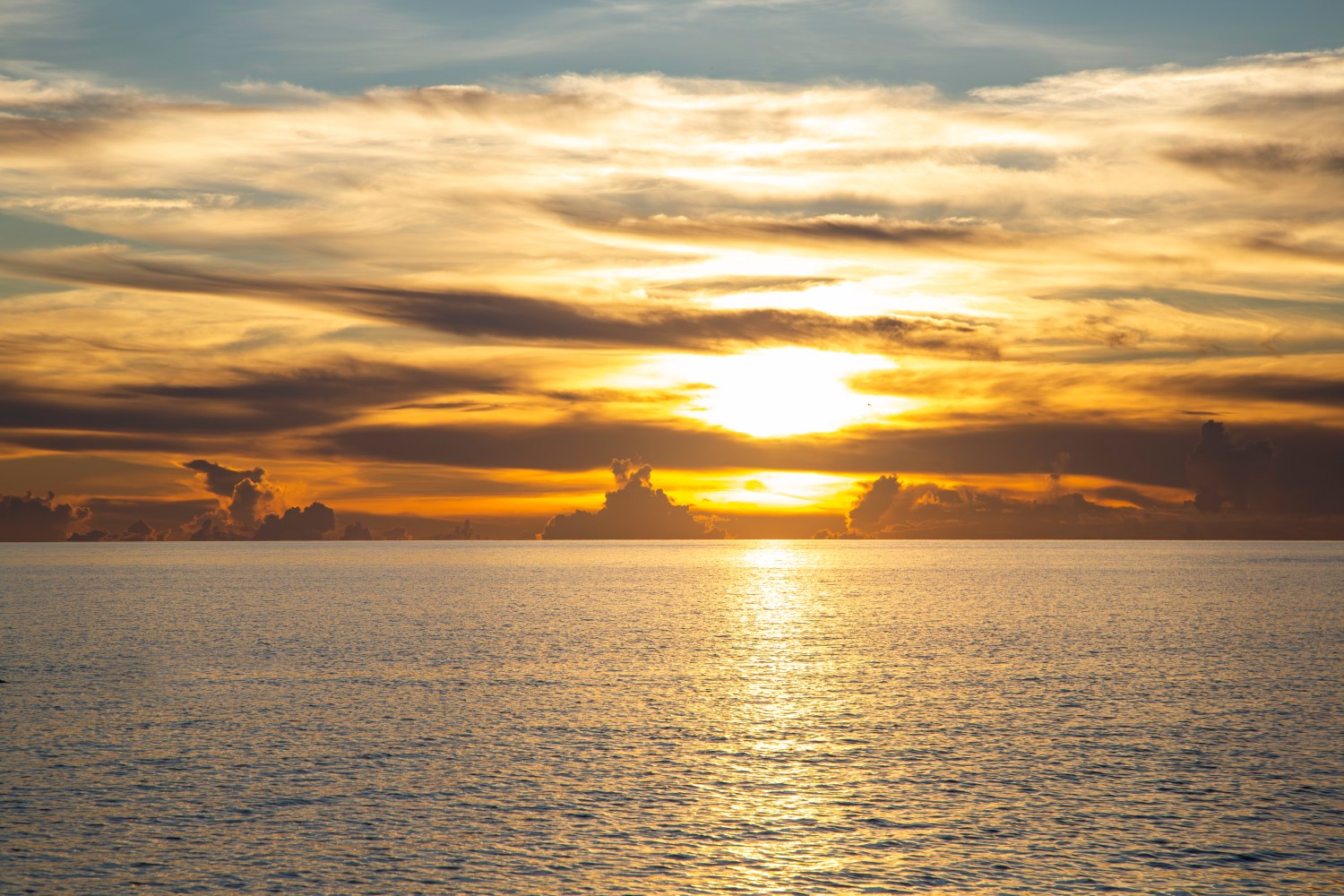 Sunset over ocean with dramatic clouds and golden sky reflections on water.