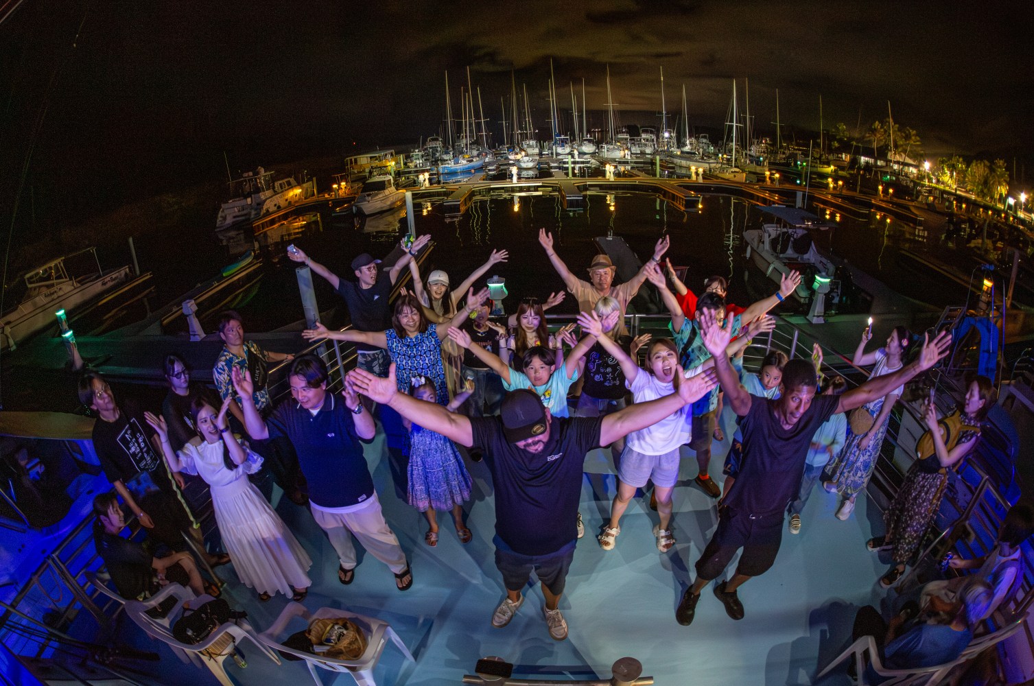 Group of people partying on a boat at night with marina in the background.