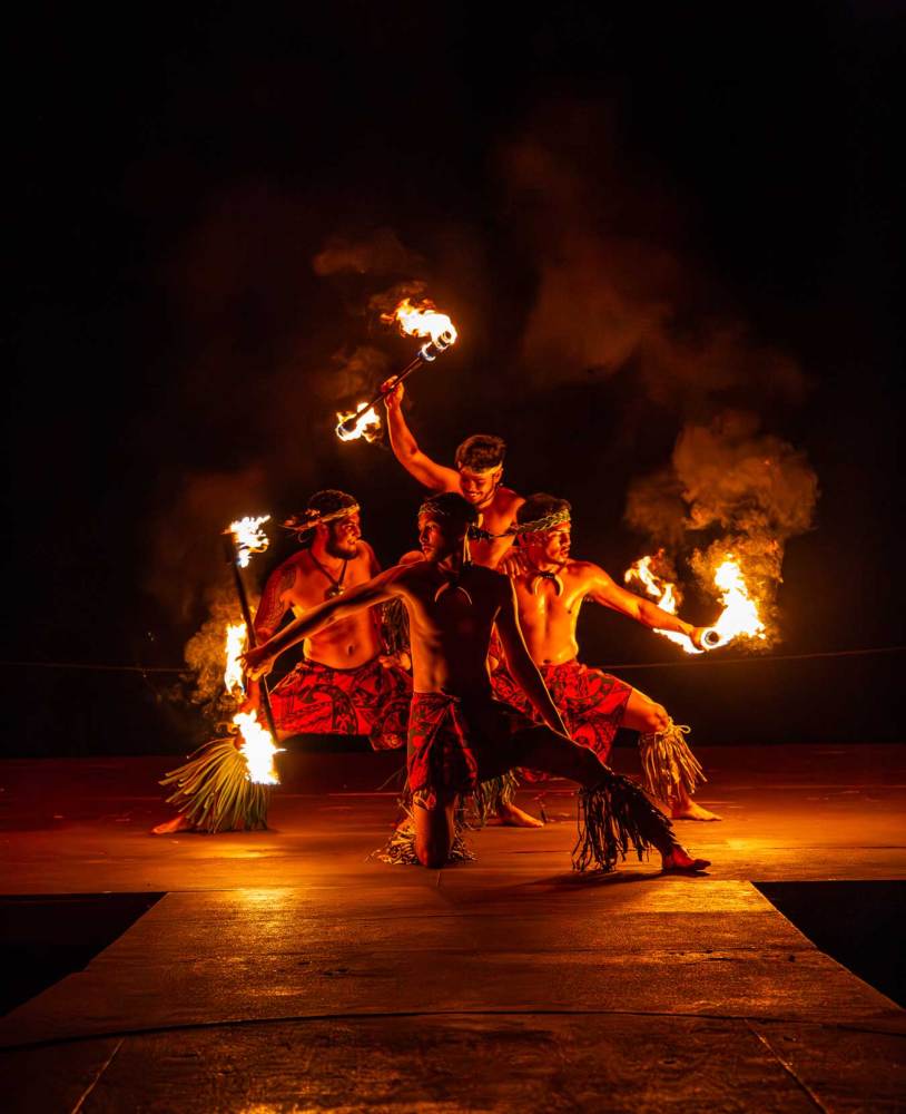 Four performers in traditional attire with fire sticks during a night performance.