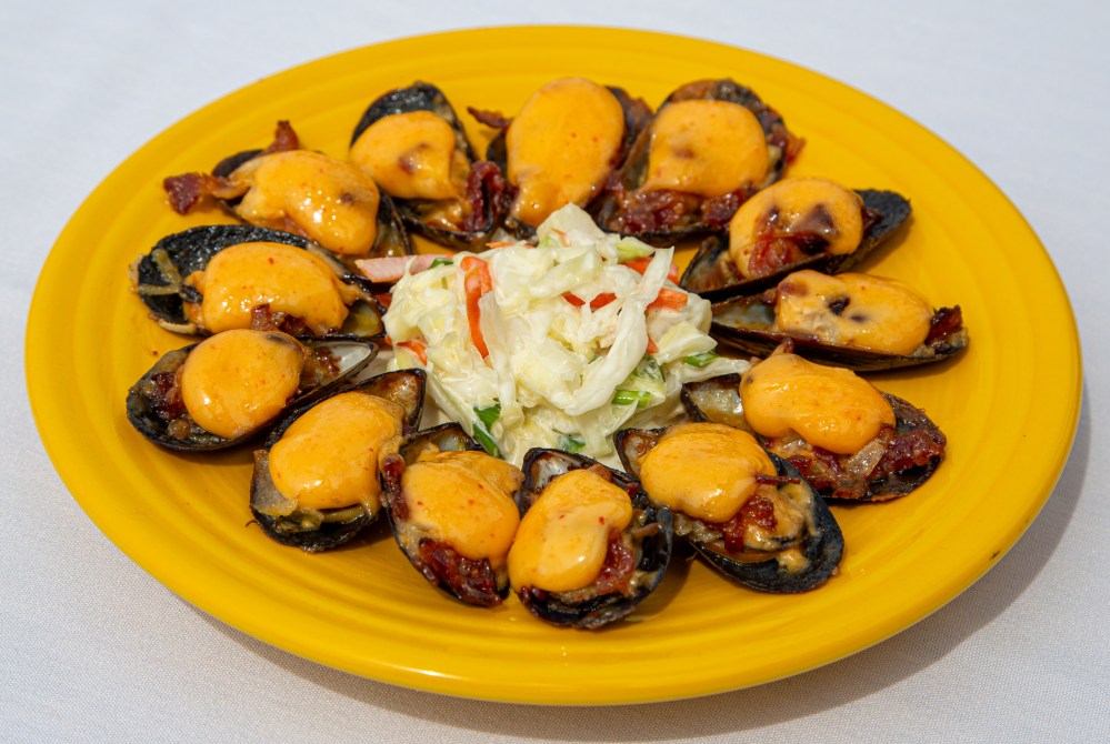 Yellow plate with baked mussels topped with cheese and a cabbage salad in the center.