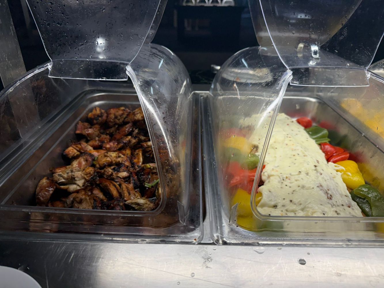 Buffet with grilled chicken and vegetables topped with creamy sauce in trays.