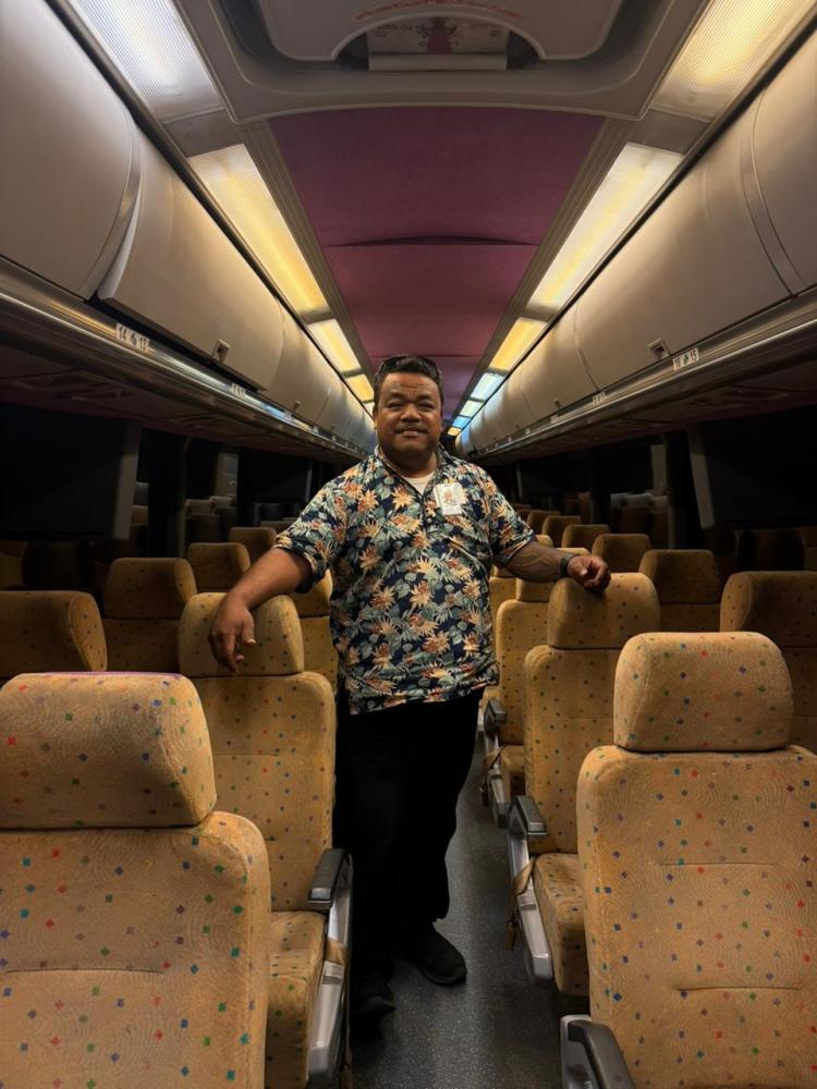 Person in floral shirt standing in aisle of an empty bus with patterned seats.