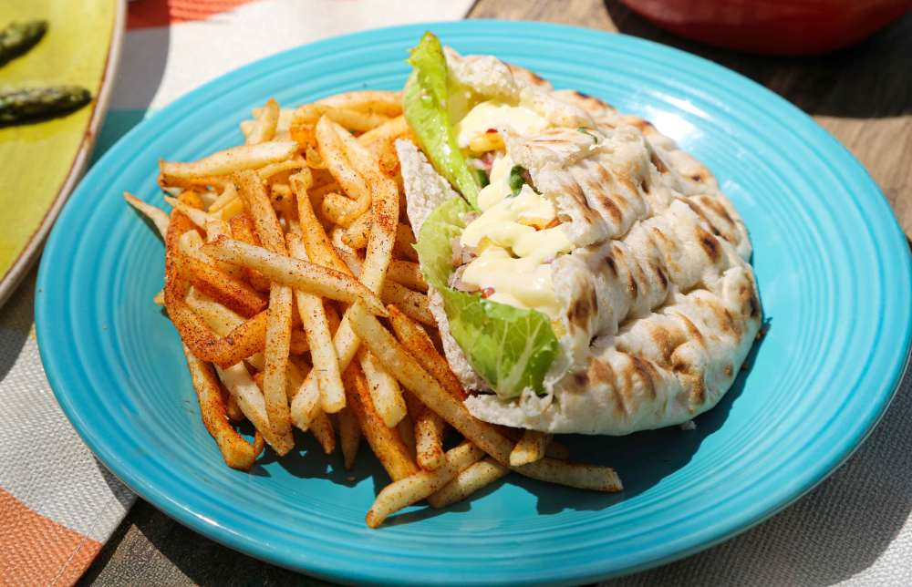 Plate of seasoned fries and a pita sandwich with lettuce on a blue plate.