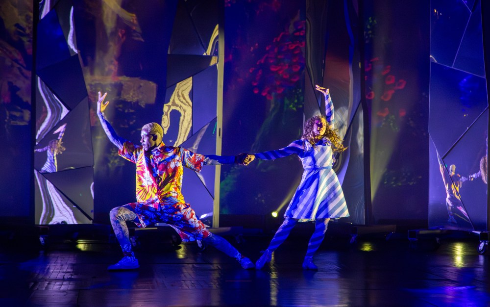Two dancers in colorful outfits perform with colorful, abstract projected backgrounds.