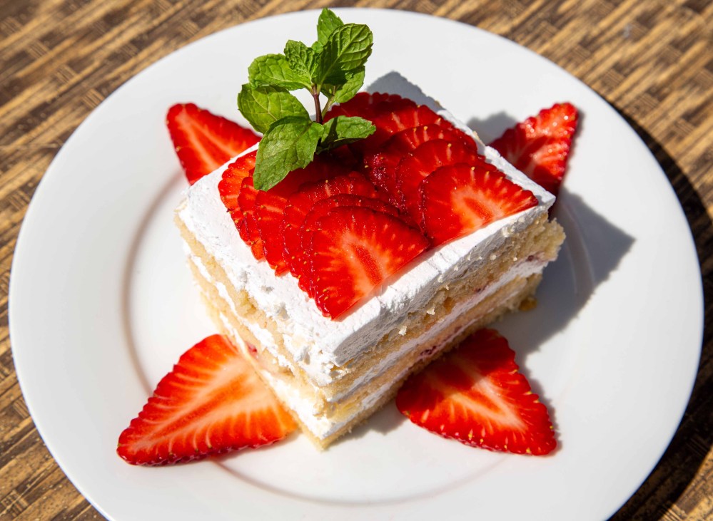 Slice of cake with whipped cream, strawberries, and mint on a white plate.