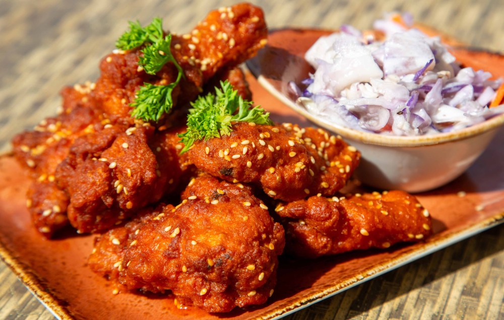 Spicy sesame-coated chicken wings with parsley next to a bowl of coleslaw on a plate.
