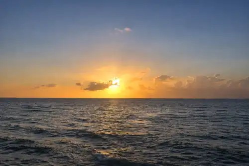 Sunset over ocean with scattered clouds and calm waves