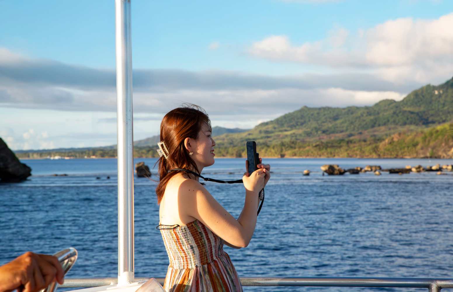 괌 선셋 디너 크루즈 데크에서 스마트폰으로 아름다운 해변 풍경을 담는 여성 관광객