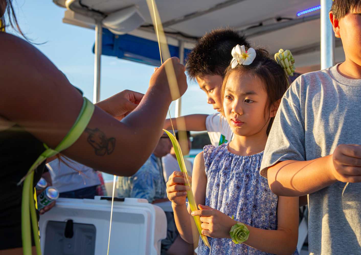괌 크루즈 체험 중 원주민 가이드와 함께 야자잎 공예를 즐기고 있는 어린이