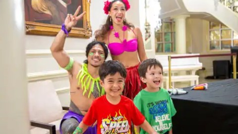 Two adults in colorful outfits pose with two smiling children in a bright room with a painting.