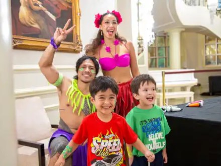 Two adults in colorful outfits pose with two smiling children in a bright room with a painting.