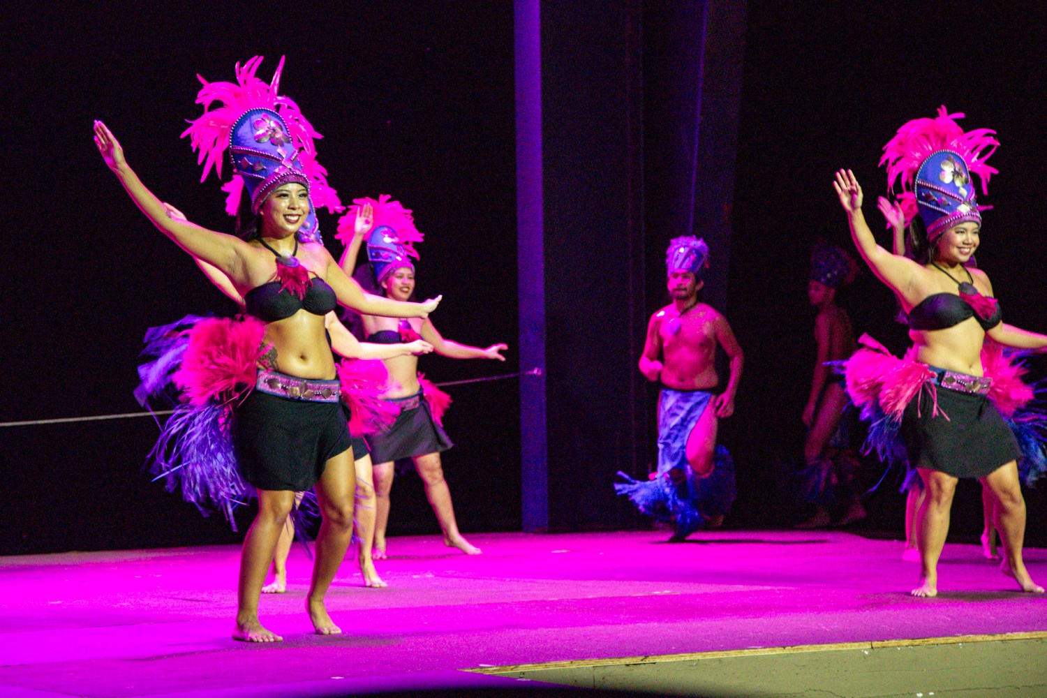 Performers in colorful costumes and headdresses dance on stage.