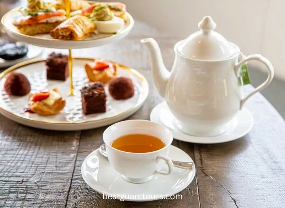 Tea set with teapot, cup, and tiered tray of pastries on a wooden table.