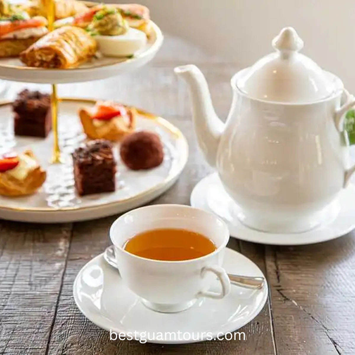 Tea set with teapot, cup, and tiered tray of pastries on a wooden table.