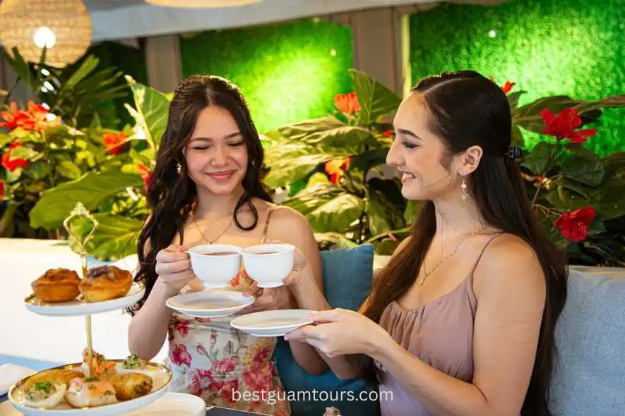 Two women enjoying tea with pastries, seated in a vibrant, plant-filled setting.