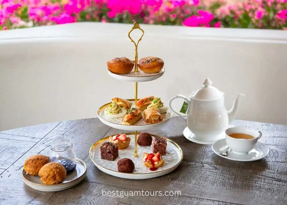 Three-tiered tray with pastries, a teapot, and a cup on a wooden table.