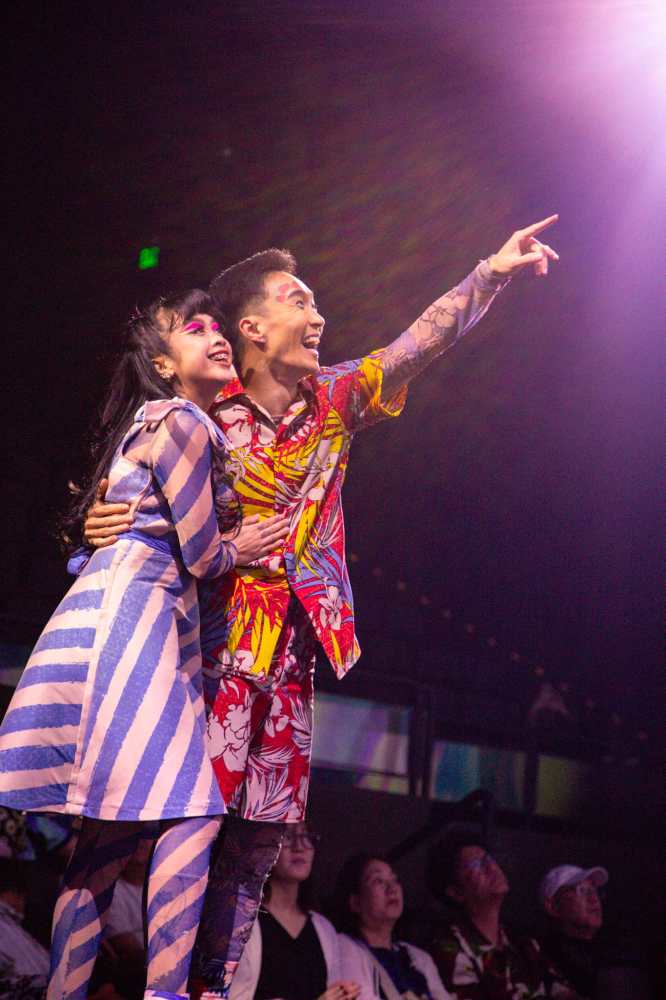 밝은 미소로 무대 위에서 관객과 소통하며 먼 곳을 가리키는 카레라 쇼 배우들