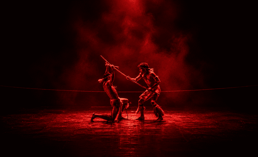 Two performers in dramatic red lighting with a pole on stage.