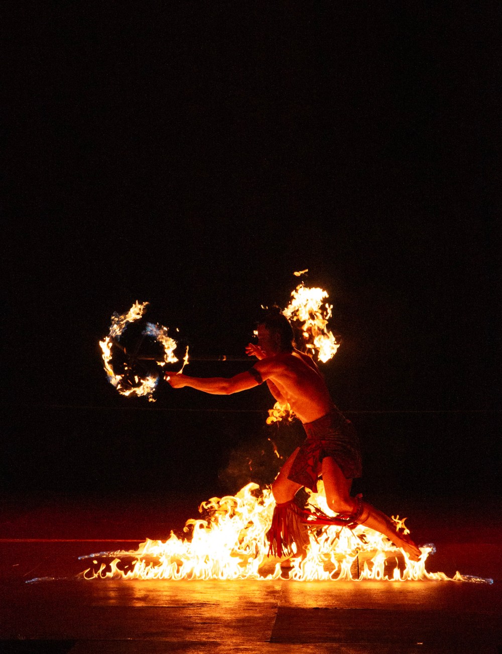 Person performing fire dance at night with flames around.