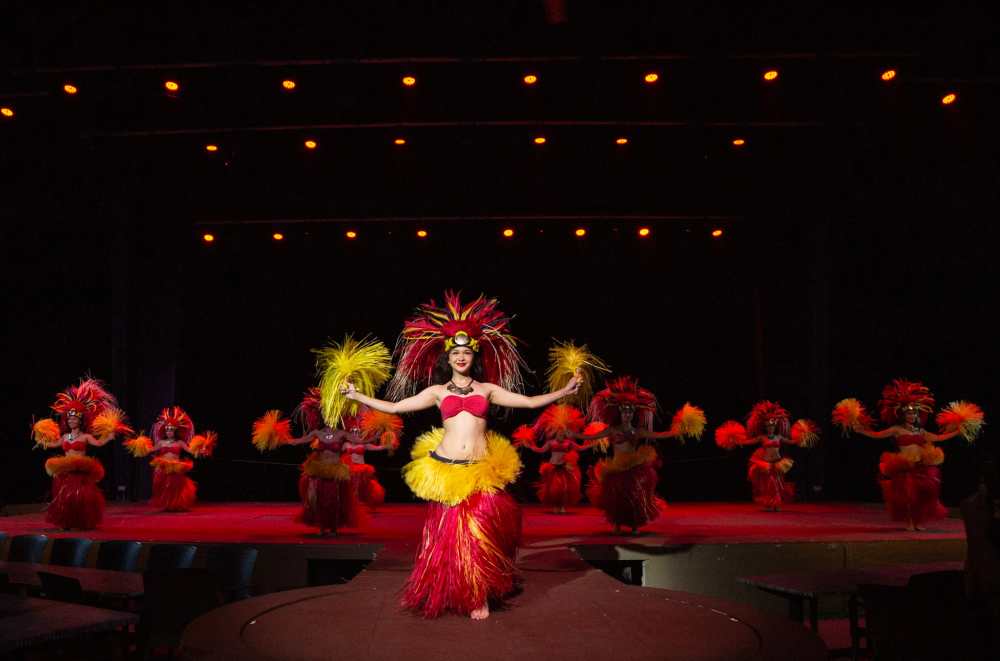 Dancers in vibrant costumes perform a traditional Polynesian dance on stage.