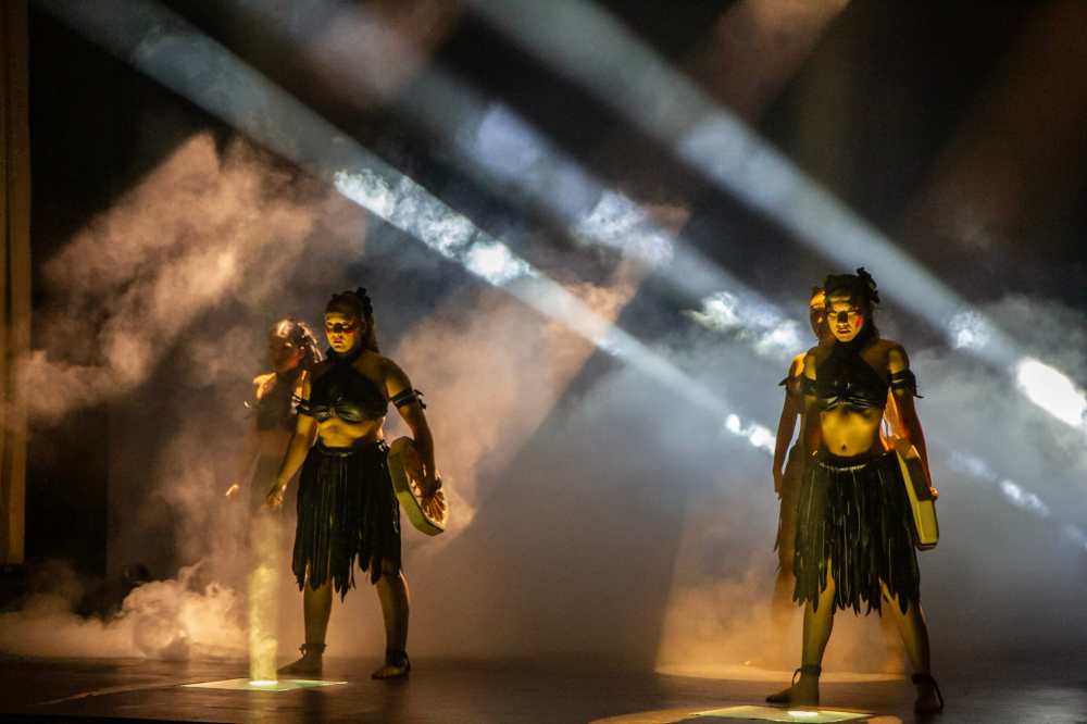 Two performers in warrior costumes on stage with dramatic lighting and smoke.