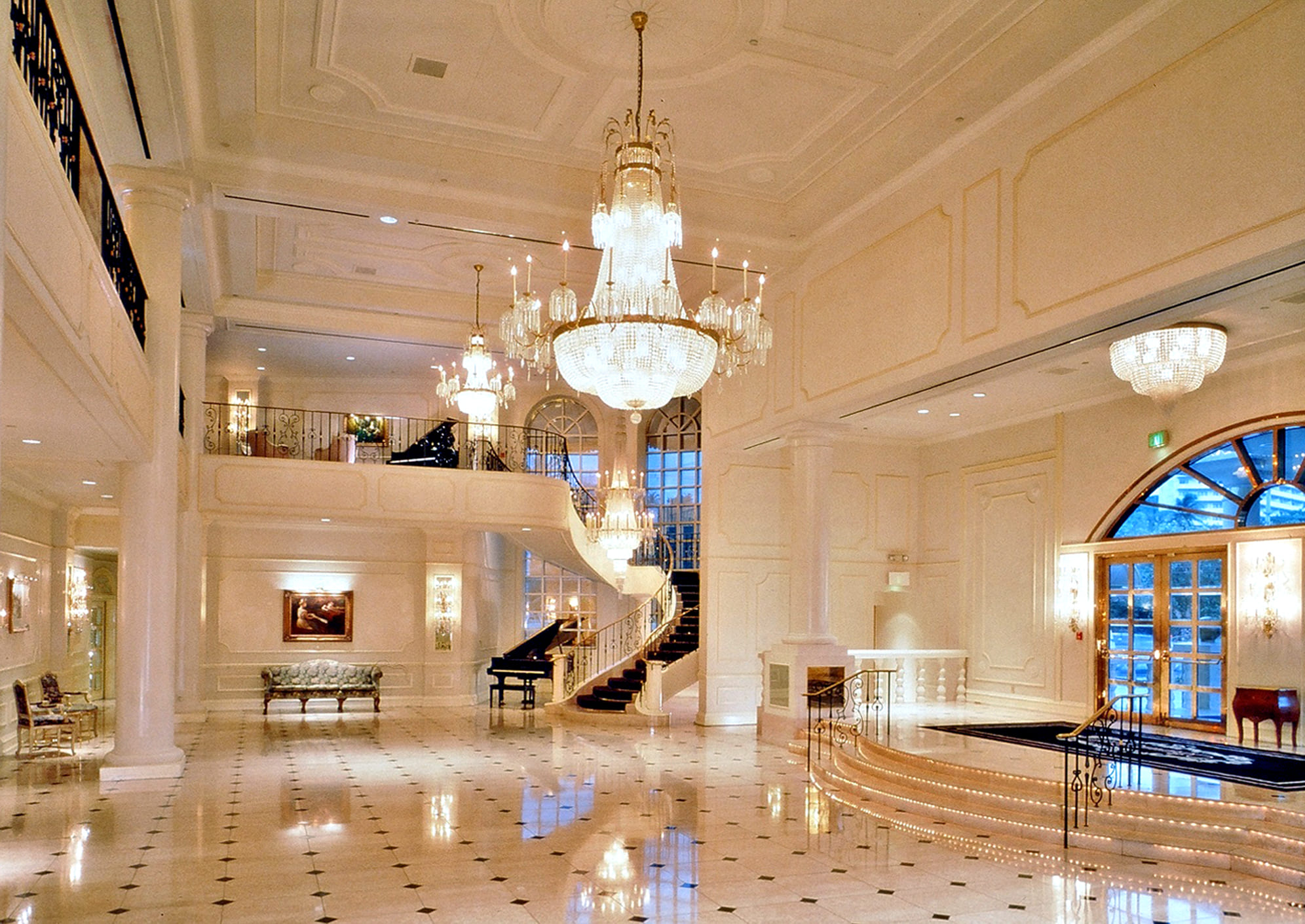Elegant hotel lobby with chandeliers, grand staircase, and marble floors.