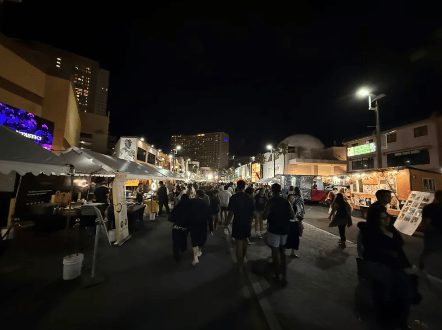 Night market with food stalls and people walking on a busy street.