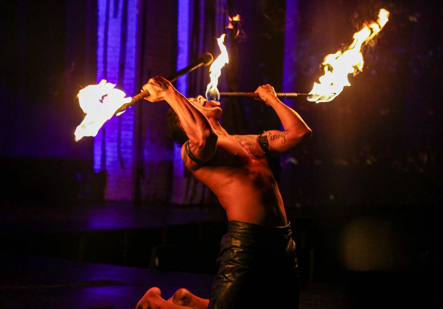 Performer kneels holding flaming torches on stage.