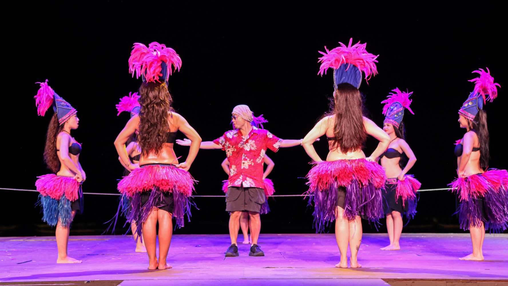 Dancers in colorful costumes performing on stage with a male instructor.