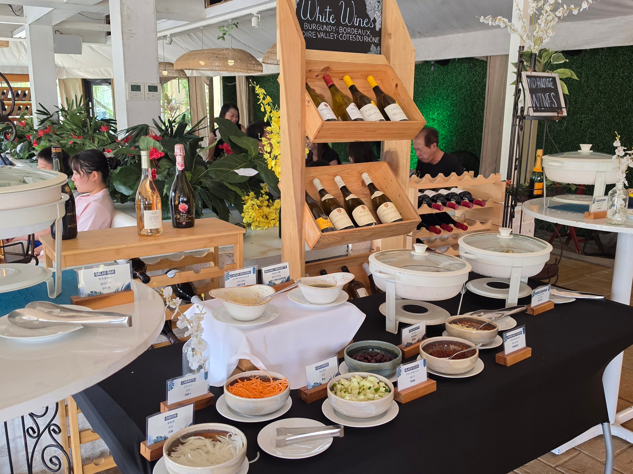 Buffet setup with wine display, salads, and condiments on black and white tablecloths.