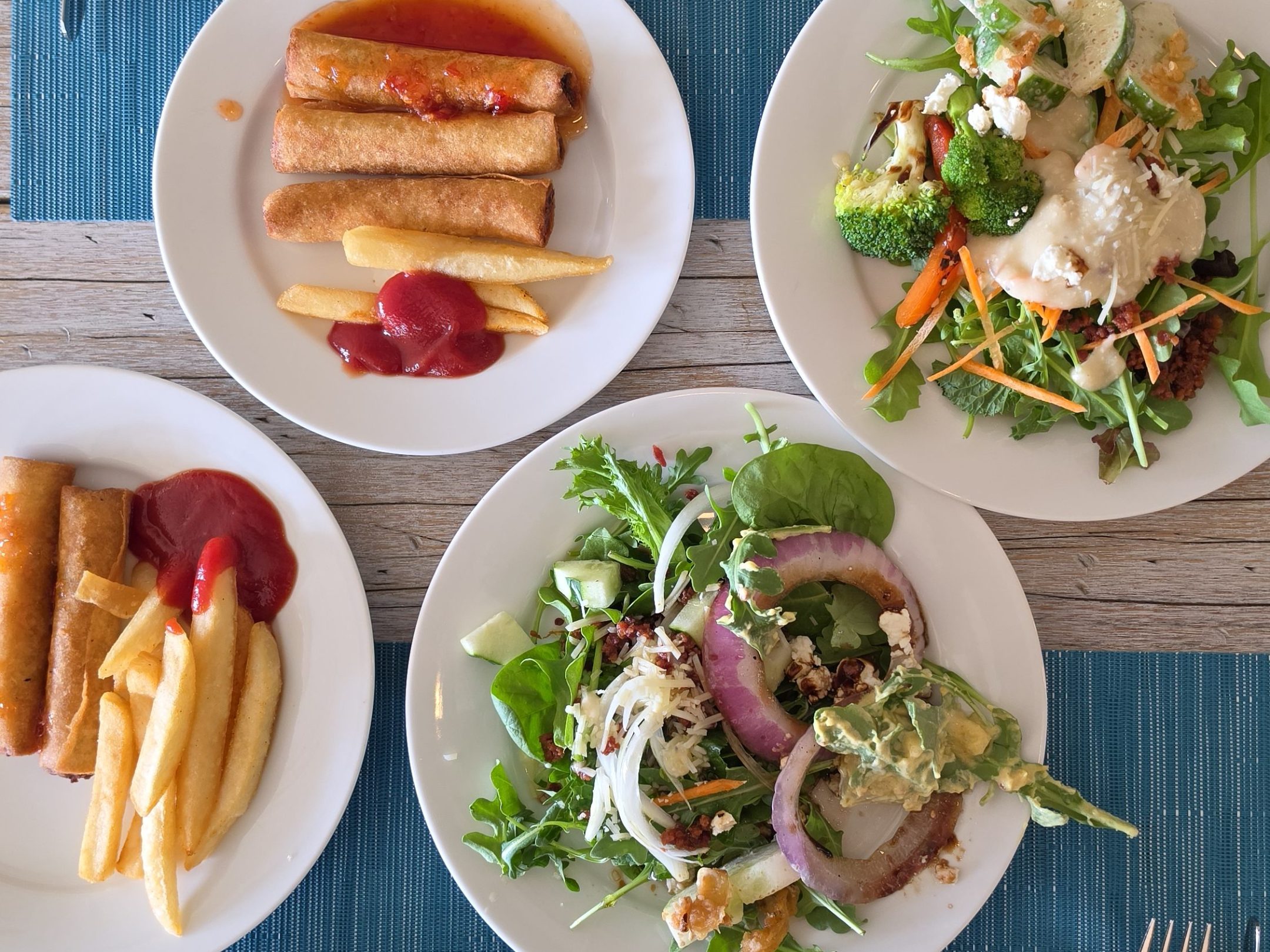 Plates of various dishes including salads, rice, and spring rolls on a table.