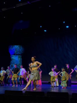 Performers in traditional costumes dancing on a dimly lit stage.