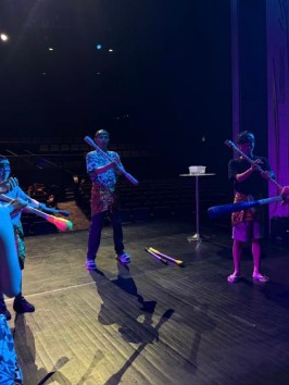 Performers in traditional attire rehearsing with sticks on stage.