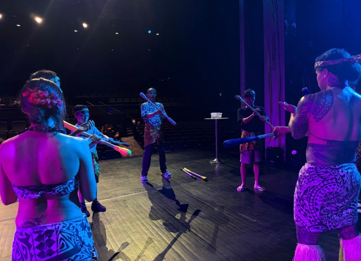 Performers in traditional attire rehearsing with sticks on stage.