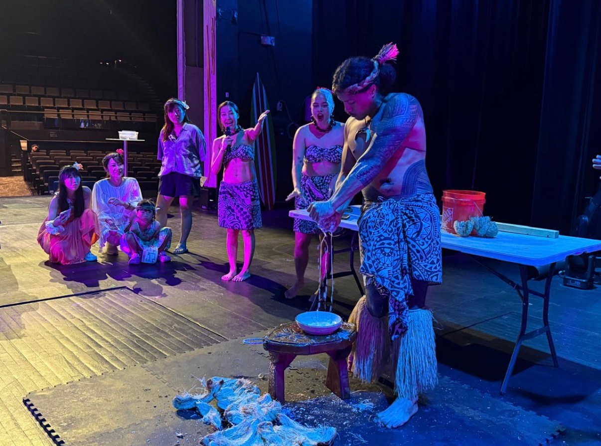People in traditional attire on stage performing a cultural demonstration.