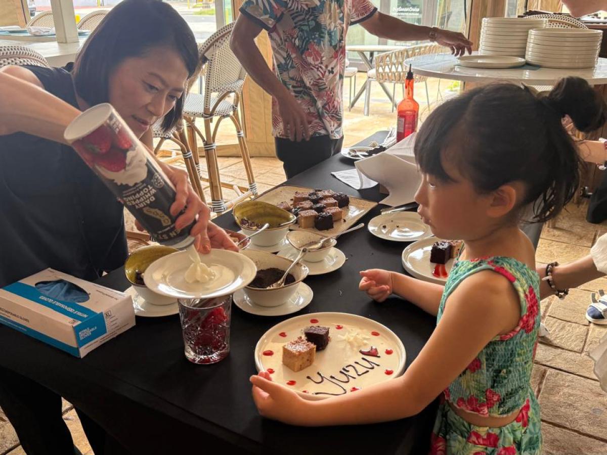 Woman pours cream on desserts as a child watches at a table.