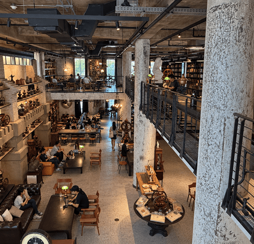 Industrial-style coffee shop with patrons, high ceiling, and two levels.