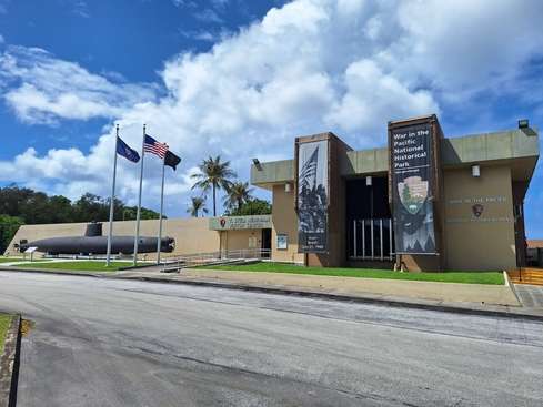 Museum building with banners and flags, palm tree, under a partly cloudy sky.